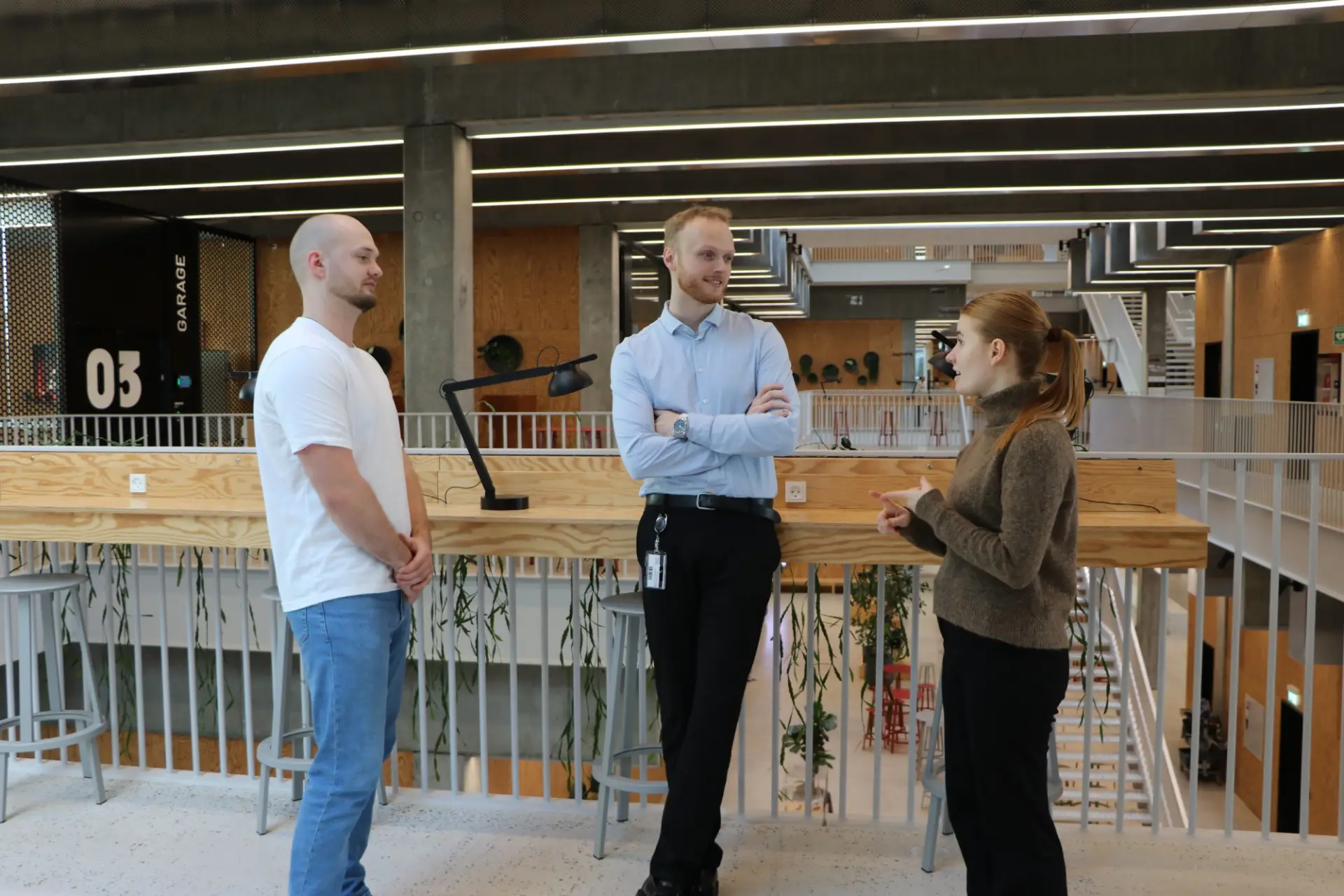 Tre fra TrailBlaze taler sammen på en gangbro i en lys universitetsbygning